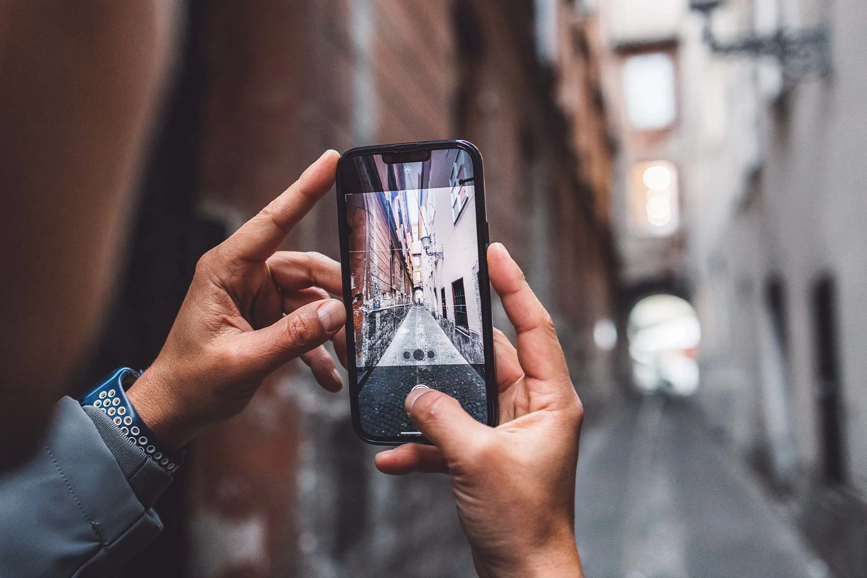 Une personne tient un smartphone et photographie une ruelle étroite avec des pavés et des bâtiments anciens. Une personne tient un smartphone et photographie une ruelle étroite avec des pavés et des bâtiments anciens.