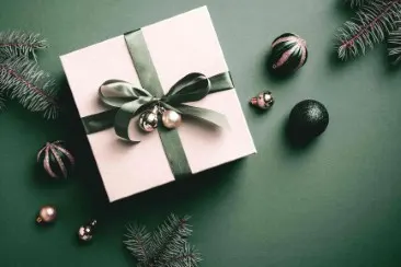 Gift with a green ribbon Gift with green ribbon and Christmas baubles on a green background, surrounded by pine branches.