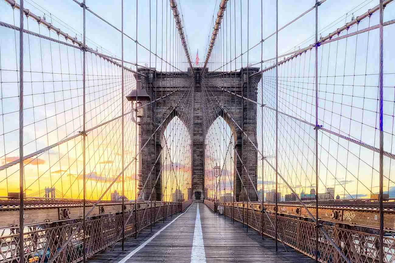 The Brooklyn Bridge at golden hour A view of the Brooklyn Bridge with its wooden walkway, steel cables, and towers during the golden hour.