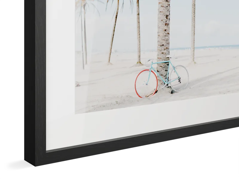 Close-up of black oak Magnet Frame with light blue vintage bicycle with red wheels parked against white wall.