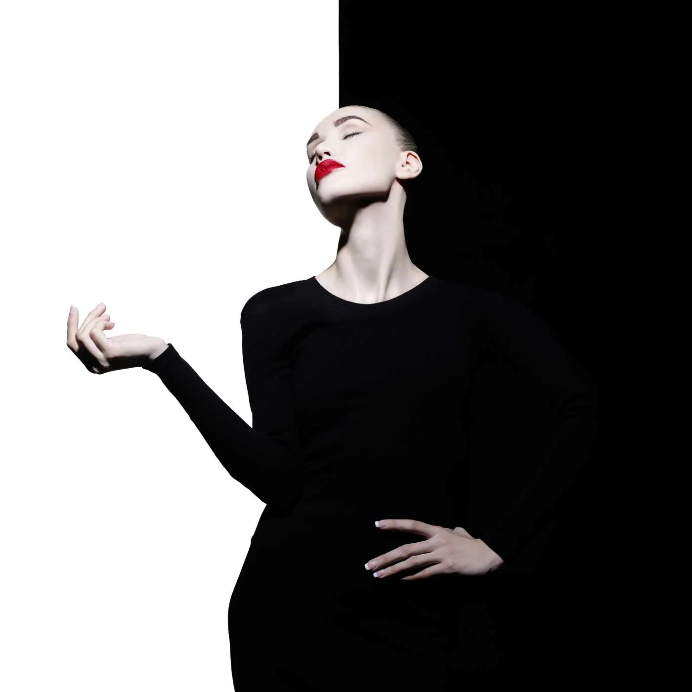 Mujer con vestido negro y pintalabios rojo delante de una pared dividida en blanco y negro. Mujer con vestido negro y pintalabios rojo delante de una pared dividida en blanco y negro.
