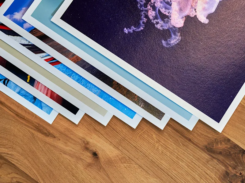 Fine Art Print 1 Several art prints with white borders lie on a wooden table, the top one shows a purple jellyfish illustration.