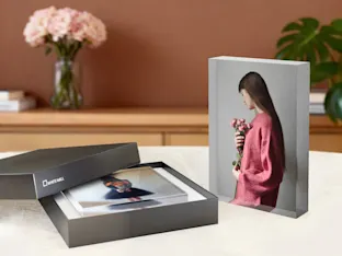 Acrylic photo block with gift box from Whitewall displayed on table with pink flowers and plant decor in background.