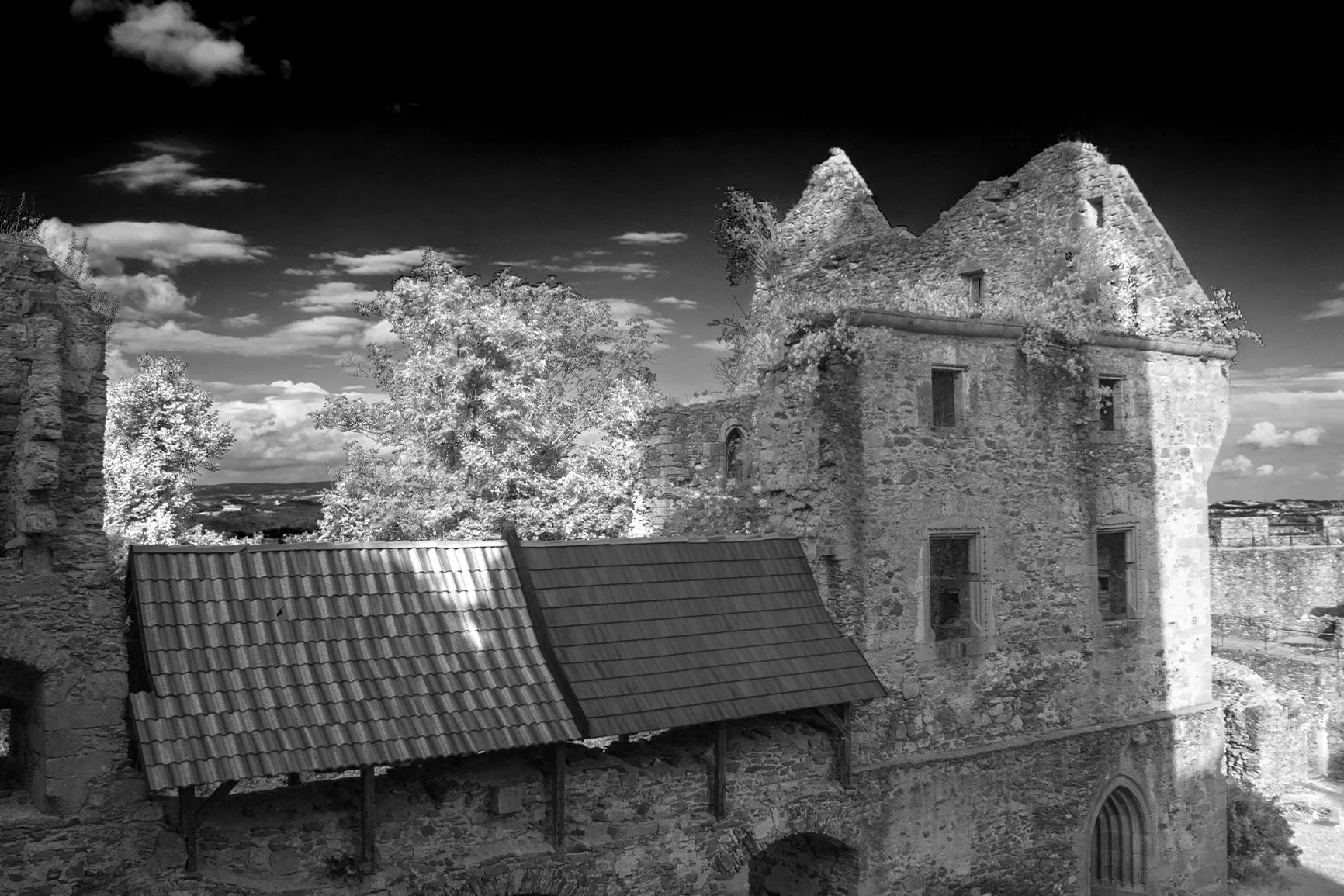 Infrared photograph of a castle ruin An infrared photograph of an old castle ruin showing stone walls, a tiled roof, and trees in the background under a cloudy sky.