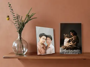Two acrylic photo stands standing on a shelf next to a vase.