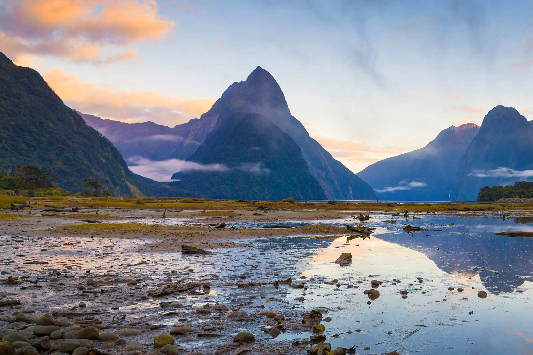 Paesaggio montuoso in Nuova Zelanda con montagne appuntite, acque tranquille e cielo nuvoloso al tramonto. Paesaggio montuoso in Nuova Zelanda con montagne appuntite, acque tranquille e cielo nuvoloso al tramonto.