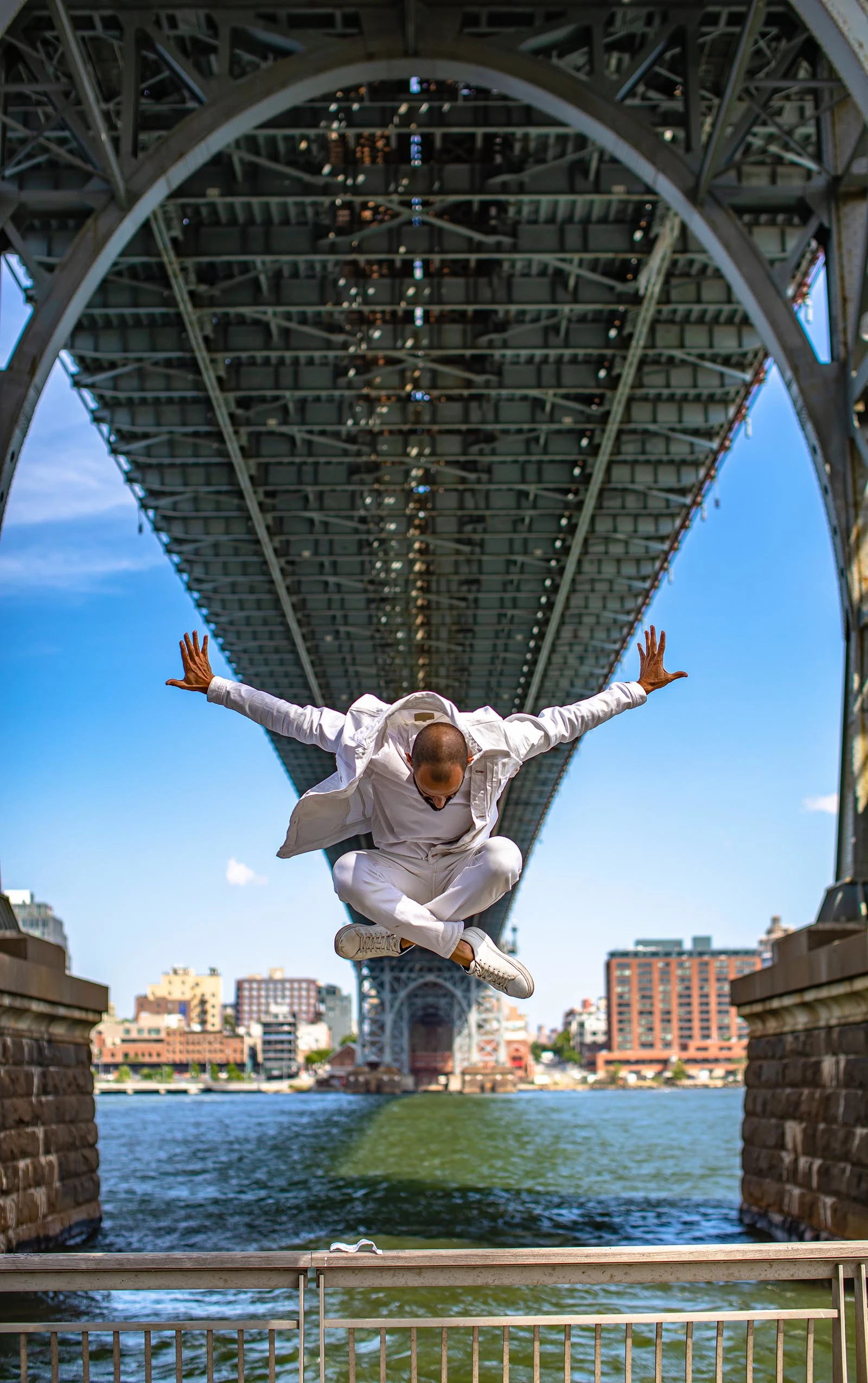 man jumping under a bridge next to a river.