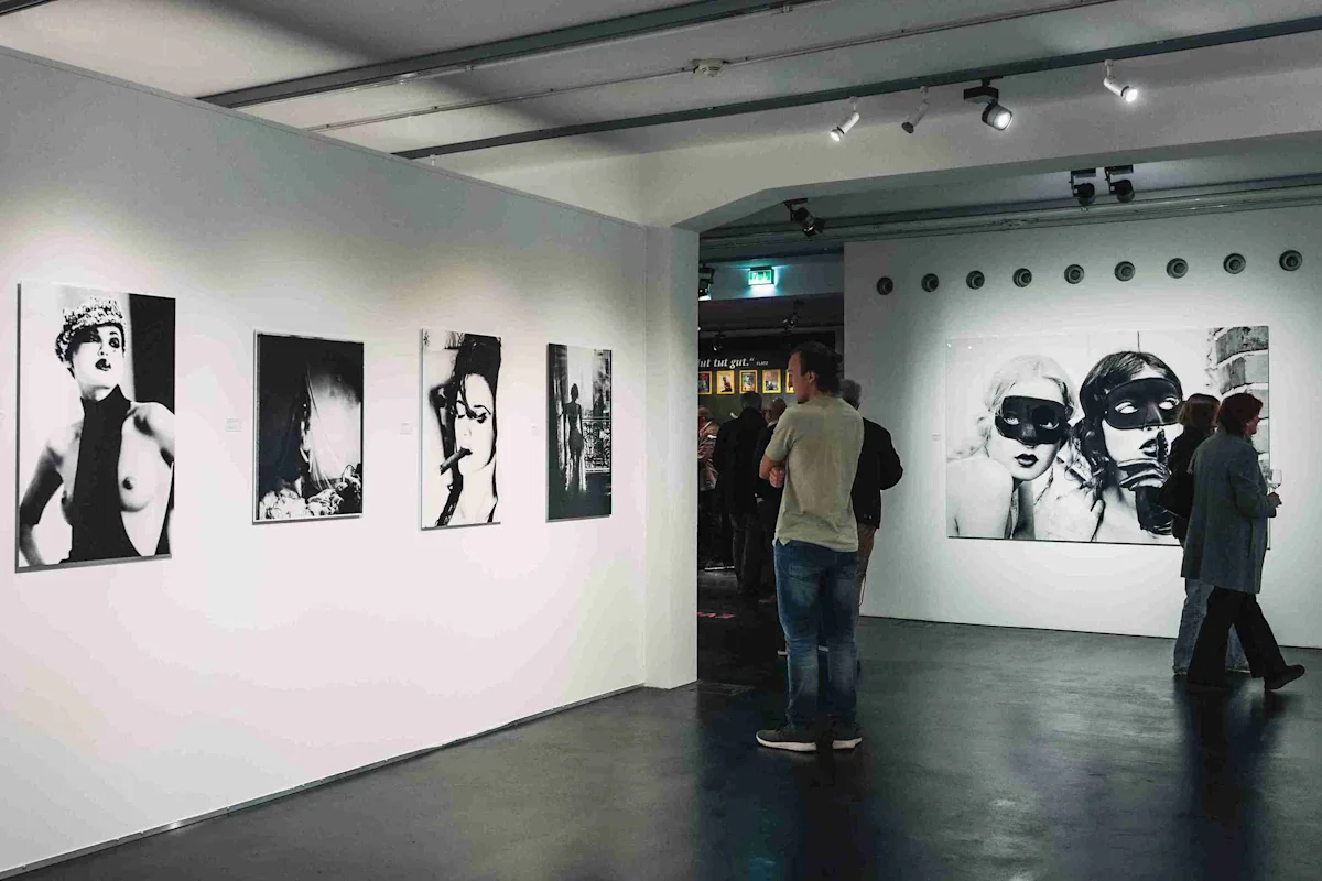 Galerie de photographies en noir et blanc Salle d'exposition avec plusieurs photographies en noir et blanc accrochées aux murs et plusieurs personnes admirant les œuvres d'art.