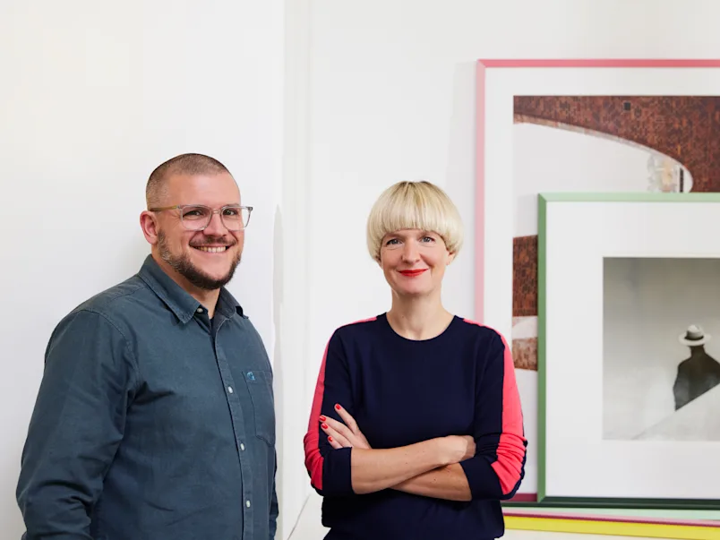 Rahmen: WhiteWall Design Edition by Studio Besau-Marguerre Bild der Designer Eva Marguerre und Marcel Besau, die nebeneinander stehen.