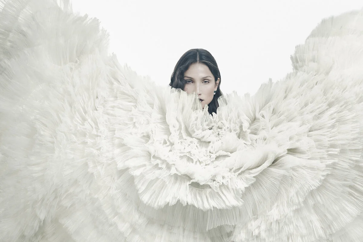 Modeporträt umgeben von dramatischen weißen Federn in einem wirbelnden Muster vor hellem Hintergrund