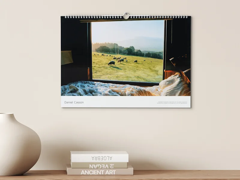 Fotokalender Kalenderphoto an der Wand: friedliche Schlafzimmerszene mit weißer Bettwäsche und Fensterblick auf grasende Schafe an einem sonnigen Hang