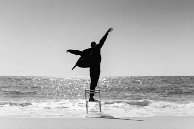 Working with existing light 2 Person on a chair by the sea, arms outstretched. Black and white shot, water glistening in the background.