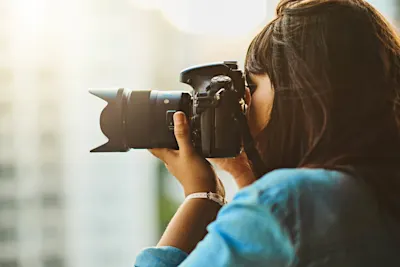A woman is holding a camera A woman with dark hair is holding a camera with a large lens and looking through the viewfinder.