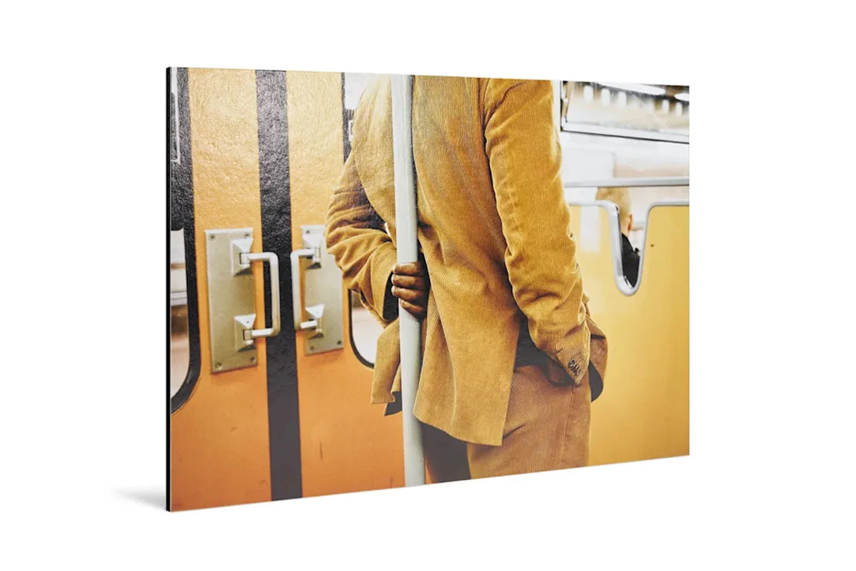 Fine Art Print on aluminum Dibond A Fine Art Print on aluminum Dibond depicts a person wearing a yellow-brown coat, standing next to a handrail in a subway car.