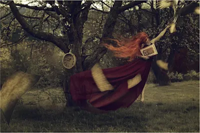 Victor Hamke – Konzeptionelle Fotografie Frau im roten Kleid hält ein Buch, Baum mit hängender Uhr, fliegende Blätter.