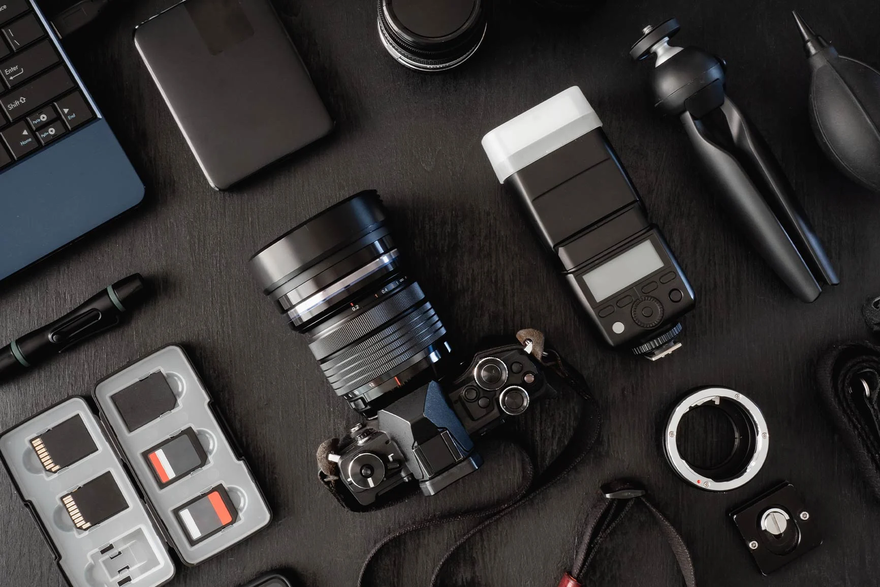 Camera with accessories A camera with a lens, flash, memory cards, tripod head, and other camera accessories on a dark background.