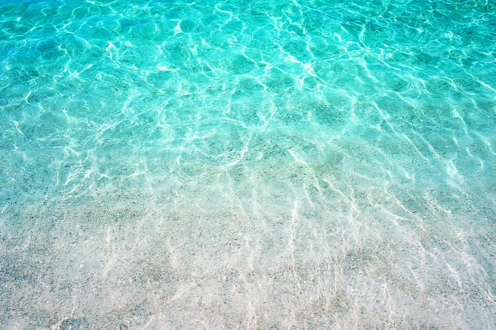 Agua clara y poco profunda, con fondo arenoso visible y reflejos del sol. Agua clara y poco profunda, con fondo arenoso visible y reflejos del sol.