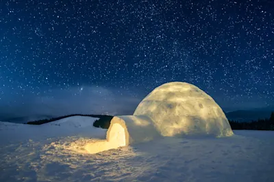 Igloo under the starry sky An illuminated snow igloo under a clear starry sky in a snow-covered landscape.