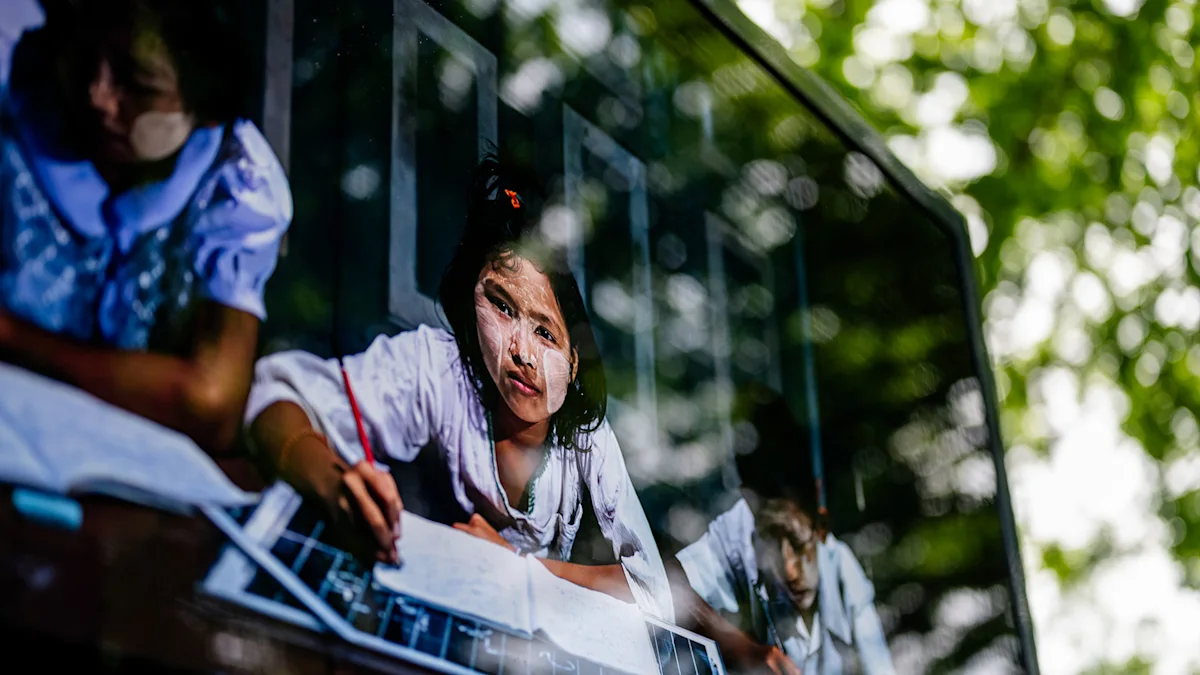 ChromaLuxe Exhibition: Rubén Salgado, “Solar Portraits” A young girl with thanaka paste on her face sits in front of table holding papers, with green trees in the background.