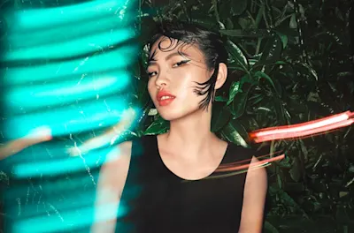 Flash Photography Basics 3 Person stands in front of green leaves with neon-colored stripes of light in blue and red in the foreground.