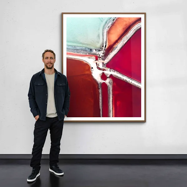 Tom Hegen One Moment WhiteWall Tom Hegen in a gallery standing in front of a printed picture from his Salt Series.