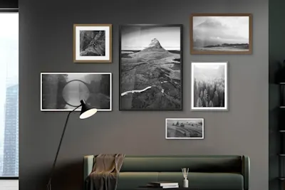 Fotografie paesaggistiche in bianco e nero Soggiorno con parete grigio scuro, divano verde, lampada da terra e sei fotografie di paesaggi in bianco e nero con cornici diverse.