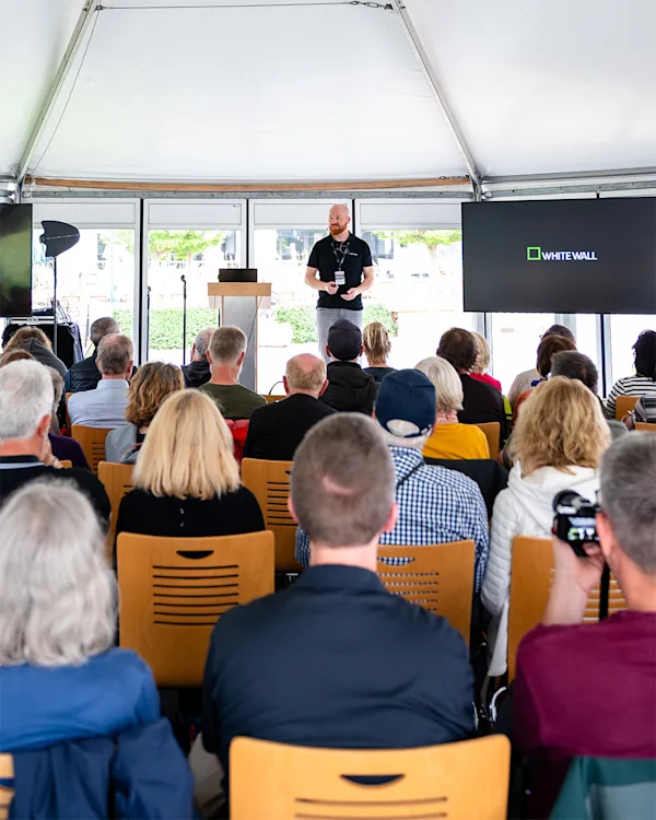 WhiteWall Expert Talk at the Horizonte Zingst Photo Festival A man in a black shirt presents at a podium to a seated audience inside a tent, with a WhiteWall logo on a screen.