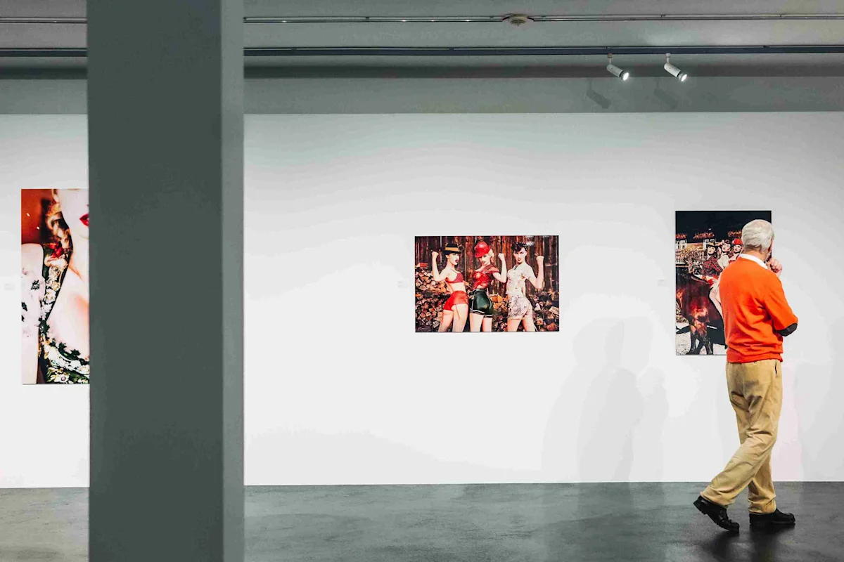 Un homme contemple des œuvres d'art dans une galerie Un homme vêtu d'un pull orange et d'un pantalon beige admire des œuvres d'art dans une galerie où trois tableaux colorés sont accrochés au mur.