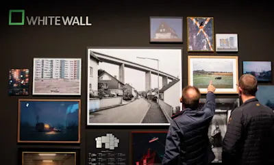 Photography communities and networks 1 Two people in front of a wall with framed photos and WhiteWall logo, one person points to a picture.