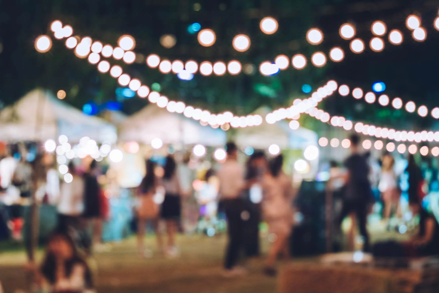 A photo from a party A blurry photo of people at a party with string lights in the foreground.