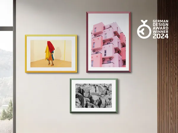 WhiteWall Design Edition Mur de galerie présentant quatre œuvres encadrées : une figure colorée, un bâtiment rose, des rochers en noir et blanc, et le logo du German Design Award 2024