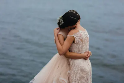 Two women hugging Two women in elegant lace dresses are hugging each other in front of a body of water.