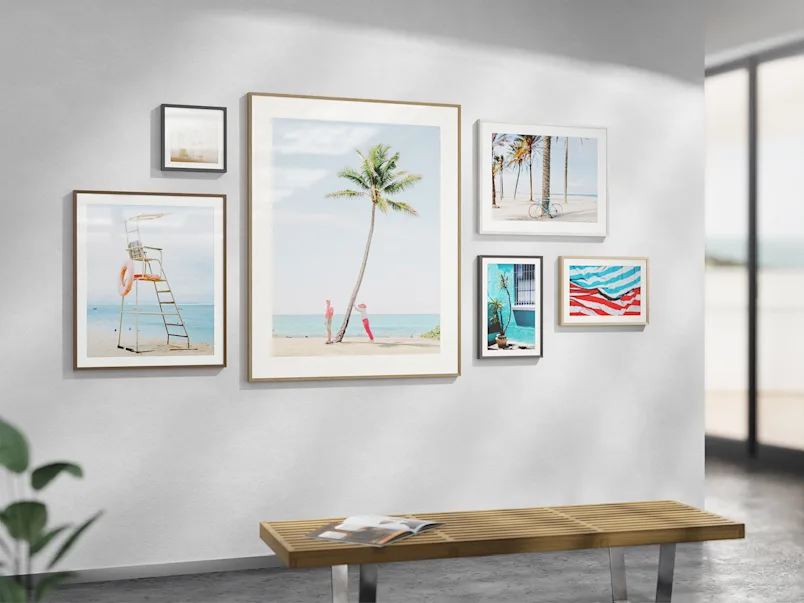 Product selector: Magnet frame options and designs Six framed beach photos in wooden magnetic changeable frames on white wall above wooden bench with open book.