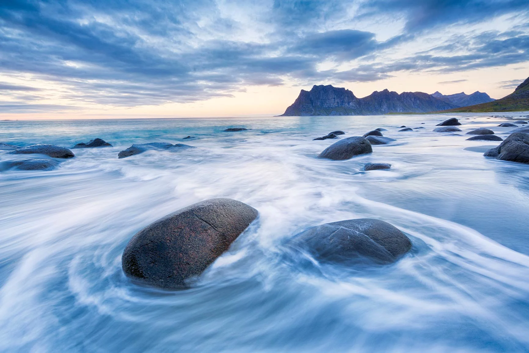 Coastal landscape with smooth rocks A coastal landscape with smooth rocks in the water and mountains in the background under a cloudy sky.