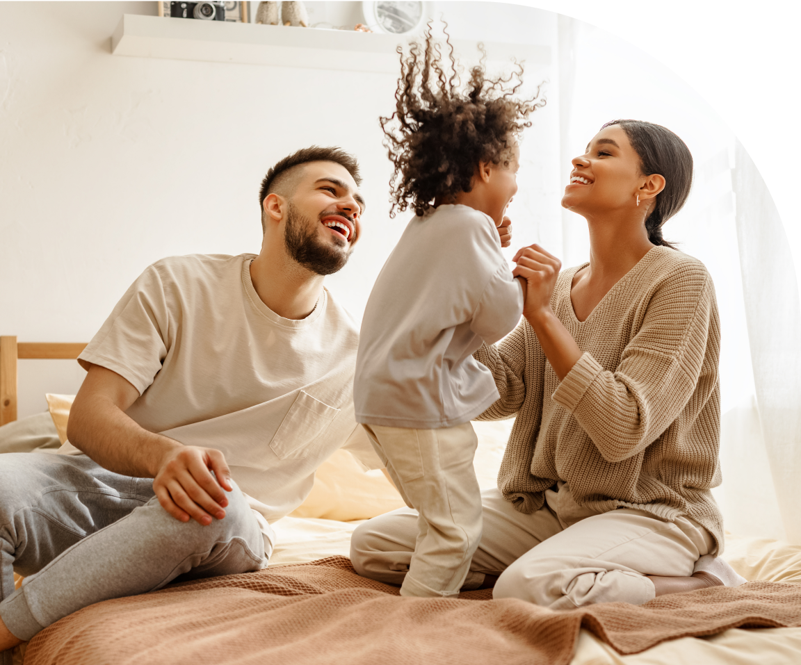 An image of a happy couple playing with their child on a bed