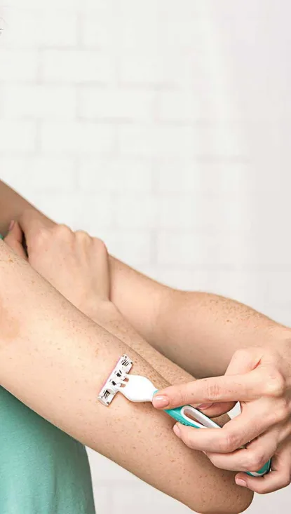 Mujer afeitándose la parte superior del brazo con la maquinilla de afeitar desechable Venus Simply 3 Sensitive
