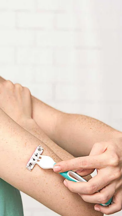 Mujer afeitándose la parte superior del brazo con la maquinilla de afeitar desechable Venus Simply 3