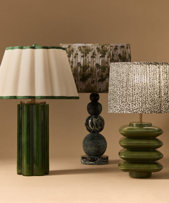 Three decorative table lamps with green and patterned bases and shades in cream, speckled, and textured designs against a tan background.