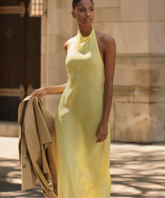 Woman in yellow halter maxi dress holding beige jacket with text "Dresses" overlaid on image