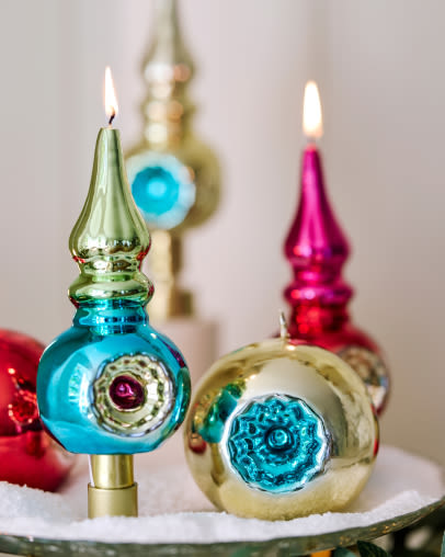 Colorful vintage glass Christmas ornaments with lit candles, featuring blue, pink, and gold metallic finishes with decorative indents.