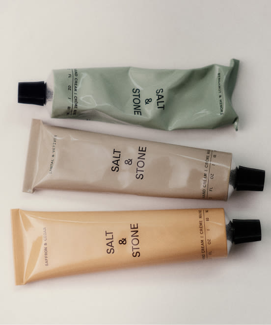Three Salt & Stone skincare tubes in sage green, beige, and peach colors with black caps arranged on white background.