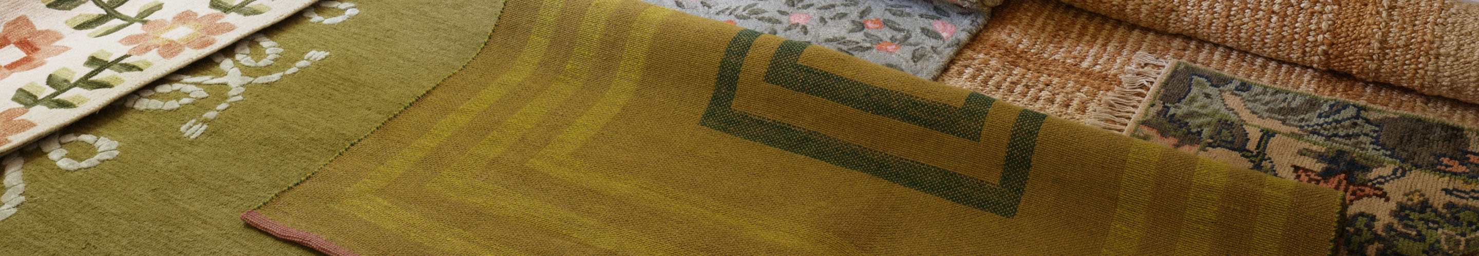 Layered decorative rugs in olive green, beige, and floral patterns with various textures and geometric designs.