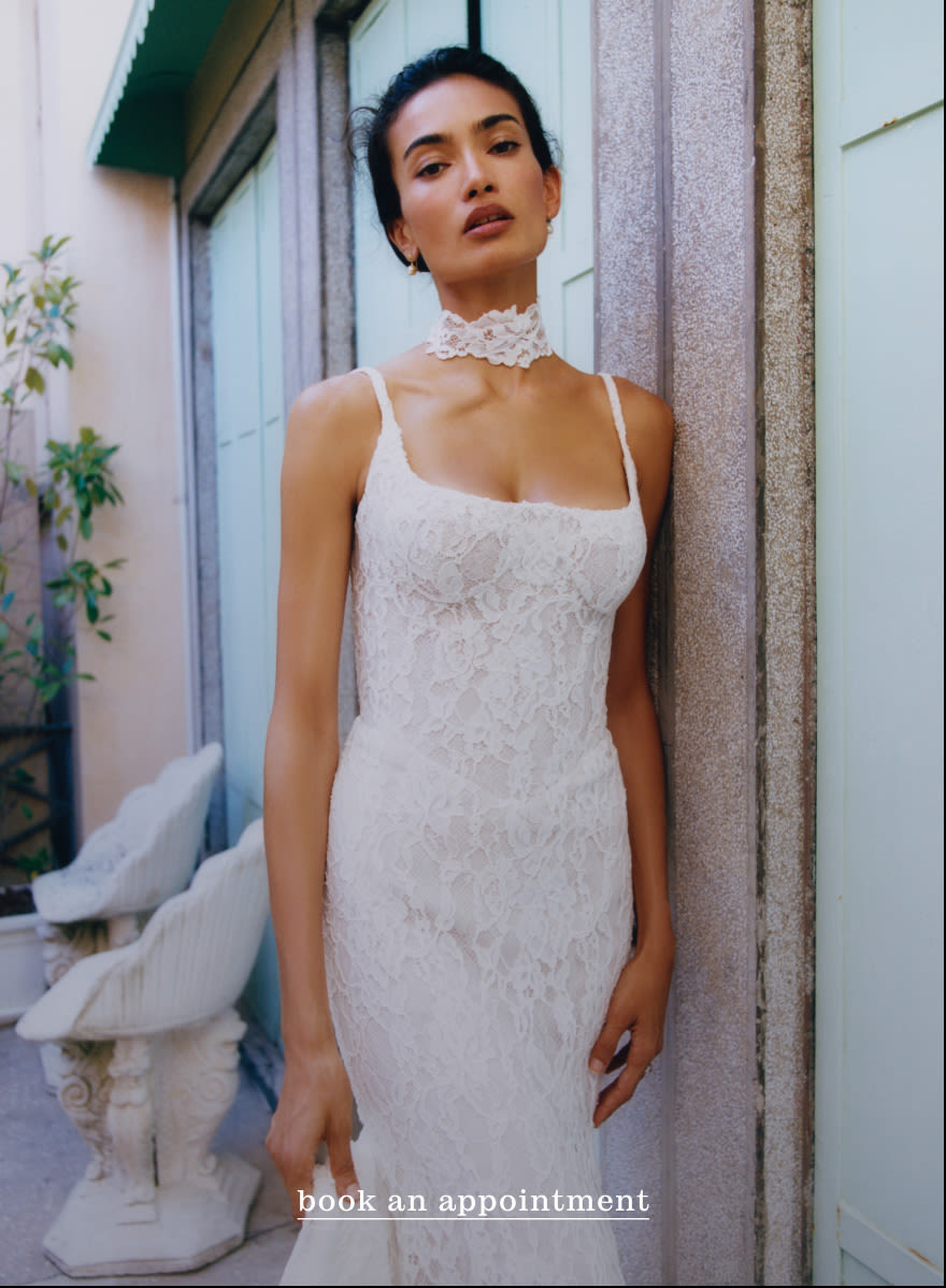 Woman in white lace dress with matching choker standing against stone column. Text reads book an appointment.