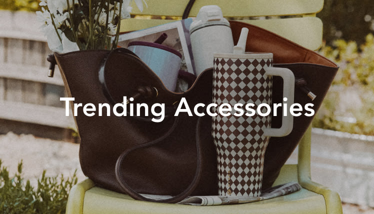 Black tote bag on yellow outdoor chair with checkered water bottle, sunglasses, and text reading Trending Accessories