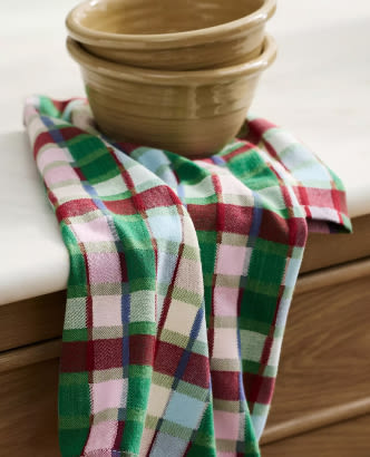 Two stacked beige ceramic bowls on a red, green, and white plaid kitchen towel draped over a wooden surface.