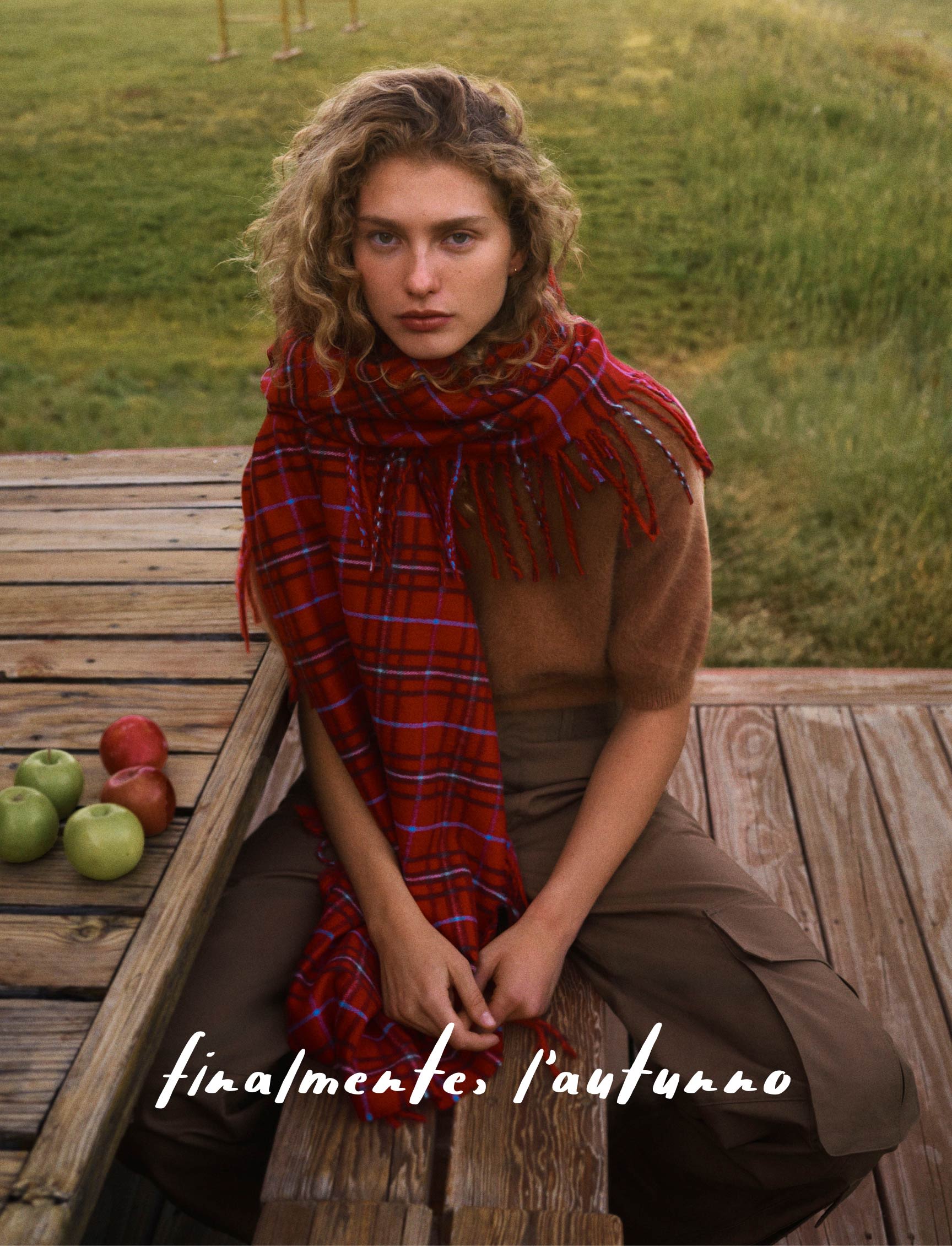 Woman in brown sweater and olive pants on wooden deck with mountain landscape, text reads "autumn, at last"