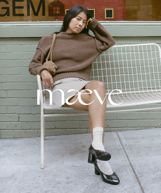 Woman in brown sweater and white shorts sitting on white metal bench against brick wall with maeve text overlay