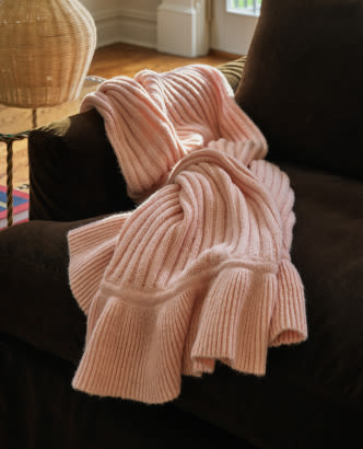 Pink ribbed knit blanket draped over a dark couch with a wicker basket in the background.