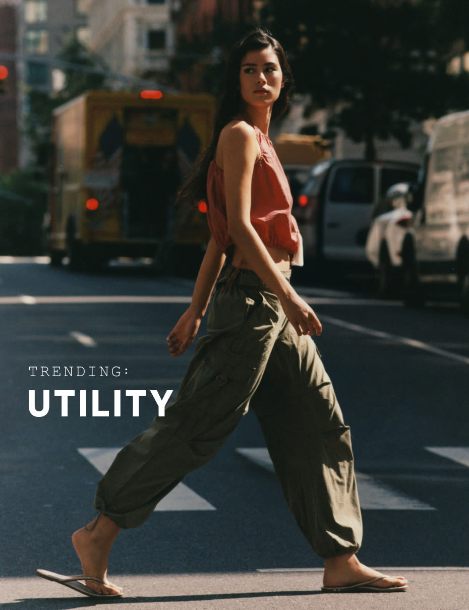 Woman in coral tank top and olive cargo pants crossing city street with text reading TRENDING: UTILITY