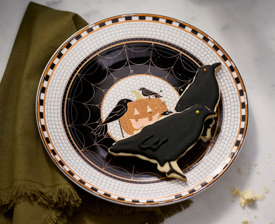 Halloween plate with black cat cookie, orange moon, ravens, and spiderweb design on white checkered rim with olive napkin.